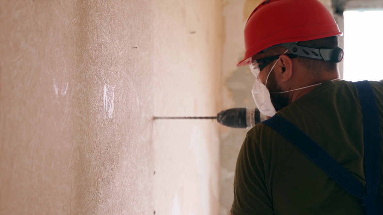 建筑工人使用旋转锤钻工作。承包商用手提钻在混凝土上打孔，拆除公寓改建和翻新的墙壁。电工统一安装布线。视频素材
