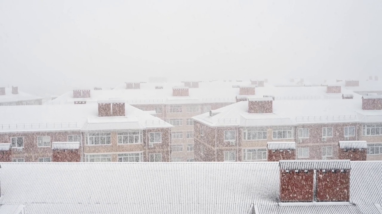 白色的雪落在住宅的屋顶上。冬天，暴风雪，雪和冰。雪地里的天空和公寓楼的屋顶。恶劣的天气条件，天气视频素材
