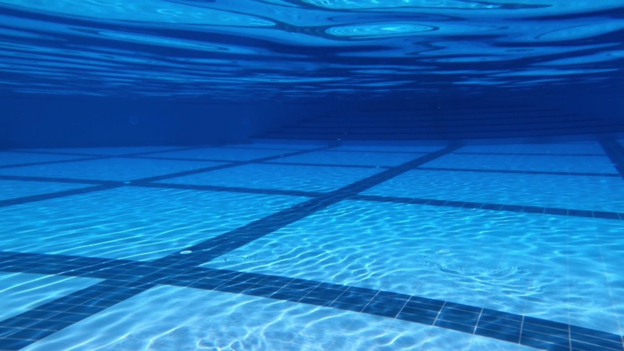 一个巨大的室外游泳池的水下视图。阳光穿过水面，在游泳池的蓝色瓷砖上创造出美丽的图案。背景或背景。视频下载