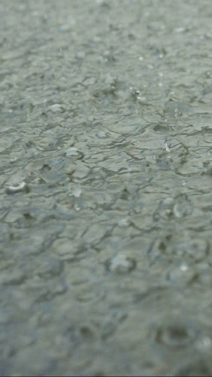 垂直视频:雨滴落进人行道上的水坑的特写。城里下起了暴雨。视频下载