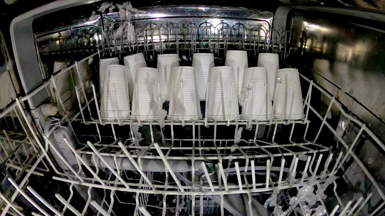 塑料盘子在洗碗机里洗。用洗碗机洗塑料玻璃杯是个疯狂的主意。查看洗碗机和一次性塑料餐具内部。慢动作内景。视频下载