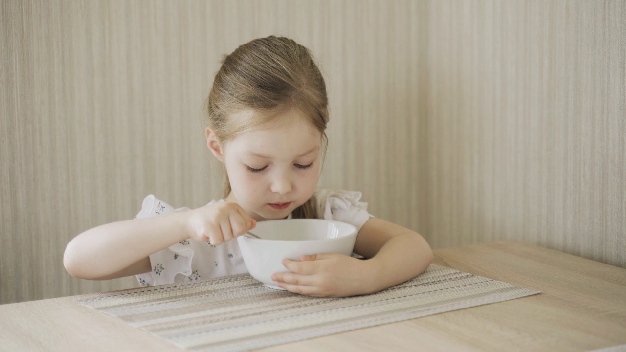 女孩坐在桌旁吃牛奶粥。视频素材