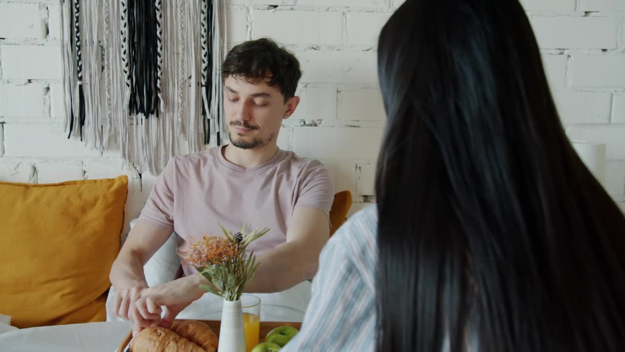 有爱心的男人在家用牛角面包喂女友，在床上喝果汁视频素材