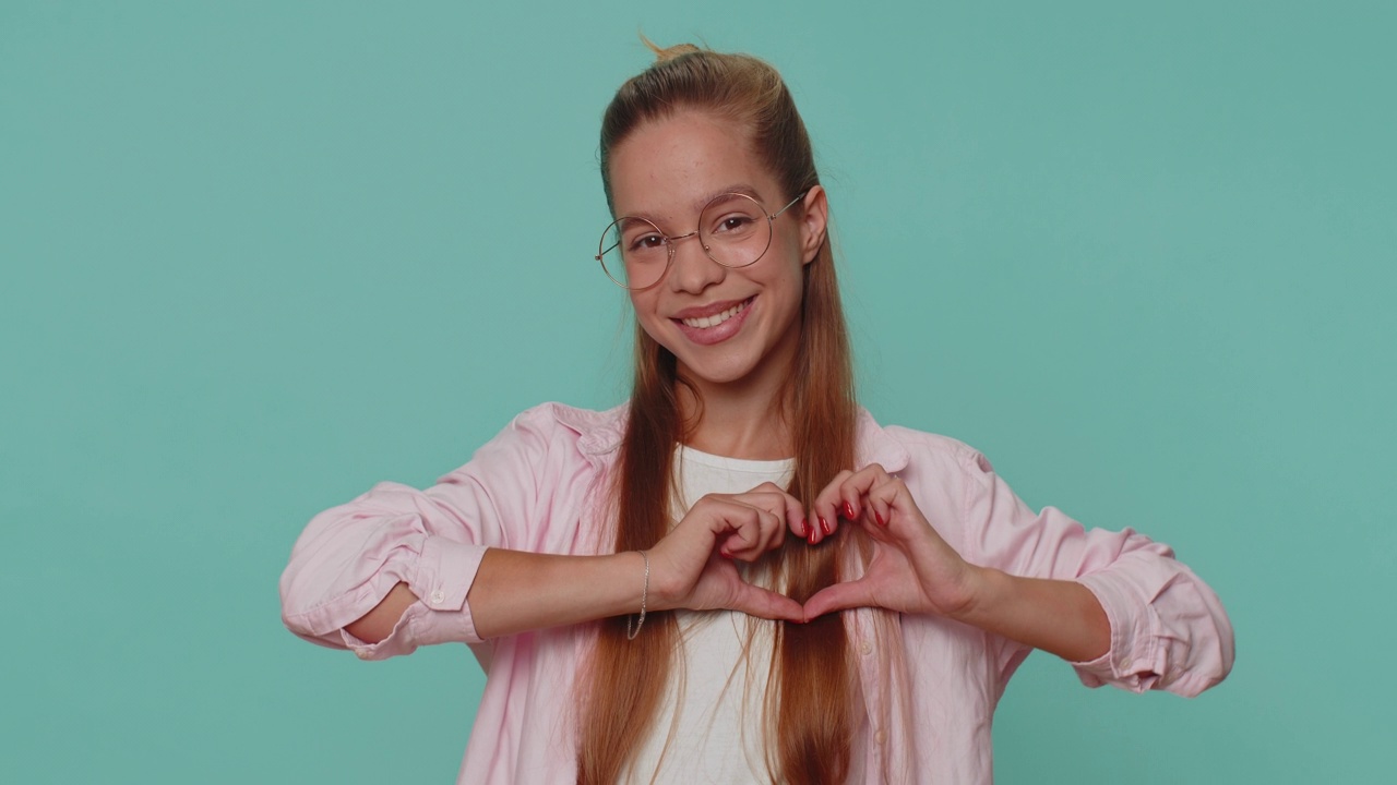 微笑可爱漂亮的十几岁女孩做心形的手势展示爱的迹象表达良好的感情视频素材