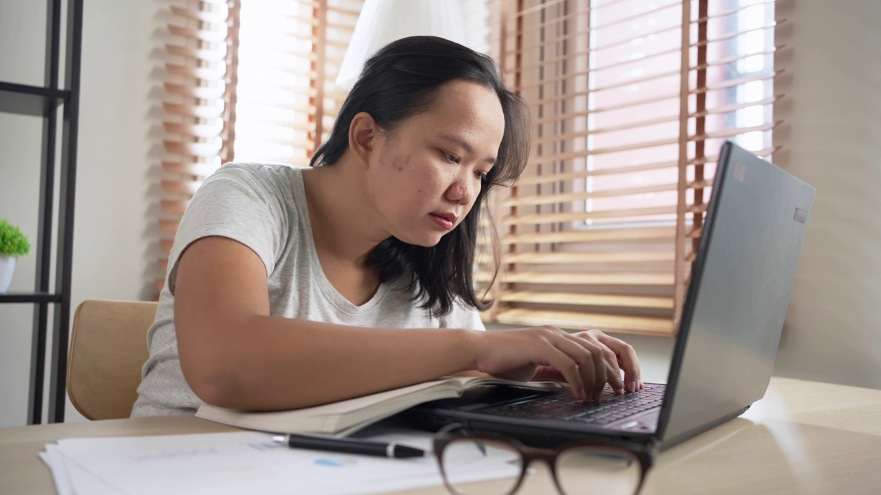 年轻的亚洲困倦女性在家里用笔记本电脑工作。努力在截止日期前完成工作的过度工作的自由职业者视频素材