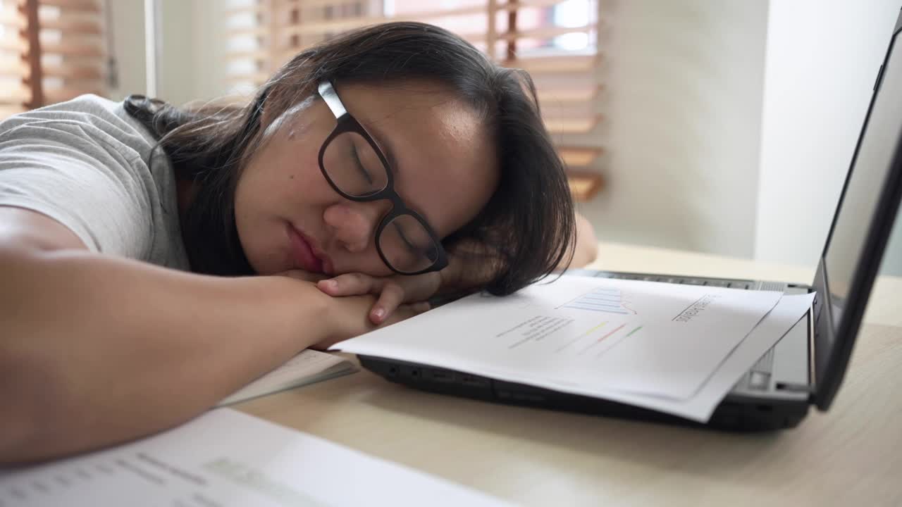 试过一位亚洲女性在家用笔记本电脑工作时睡在桌子上。在自由职业中工作到最后期限视频素材