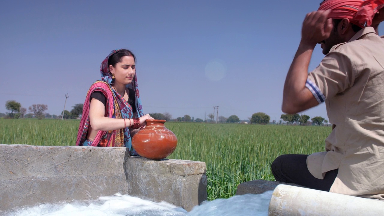 迷人的乡村女子正从管井里用陶罐装满日常用水，这是印度乡村的景象视频素材