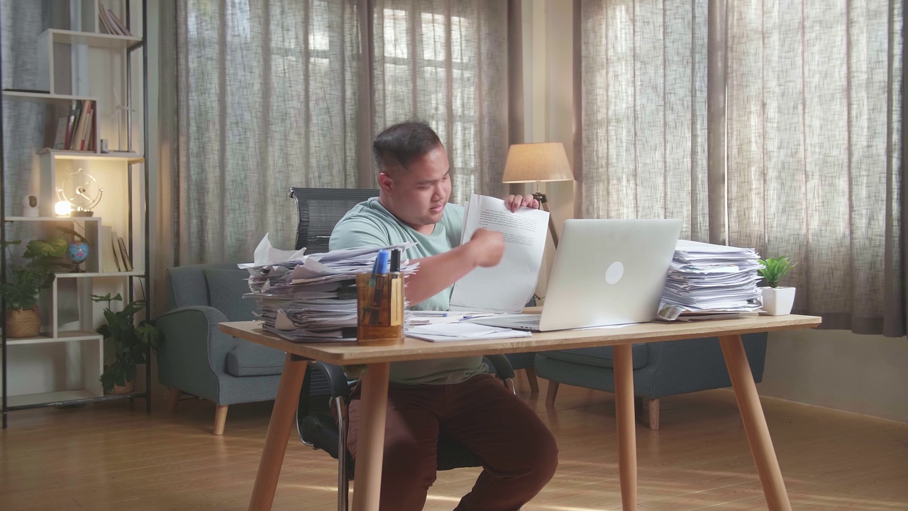 亚洲胖子在办公室用笔记本电脑视频通话时，手里拿着解释工作的文件视频下载