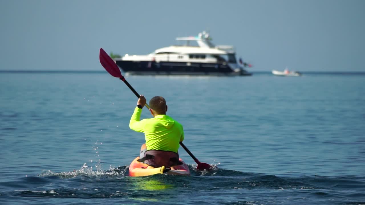海人皮艇。运动员在夏天日落时划皮艇在海里游泳。健康强壮的男性喜欢在假期进行户外运动和水上运动。慢动作视频下载