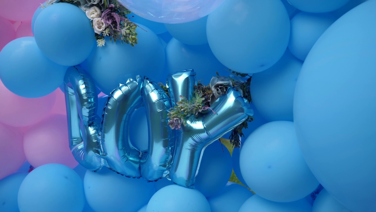 在一场性别揭牌派对上，来自蓝色氦气球的字母在彩色气球的背景下组成了“男孩”这个词视频下载
