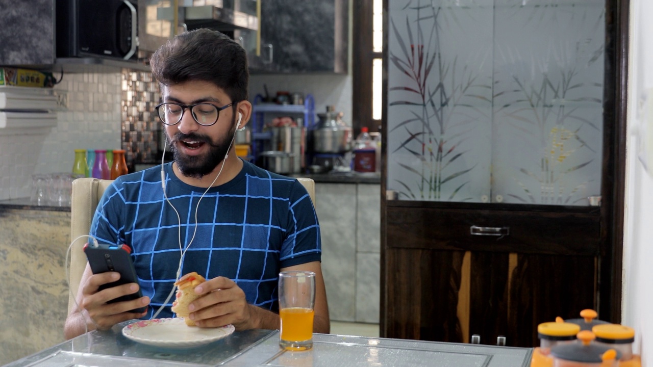 留着胡子的印度人戴着白色耳机，一边吃早餐一边欣赏音乐视频素材