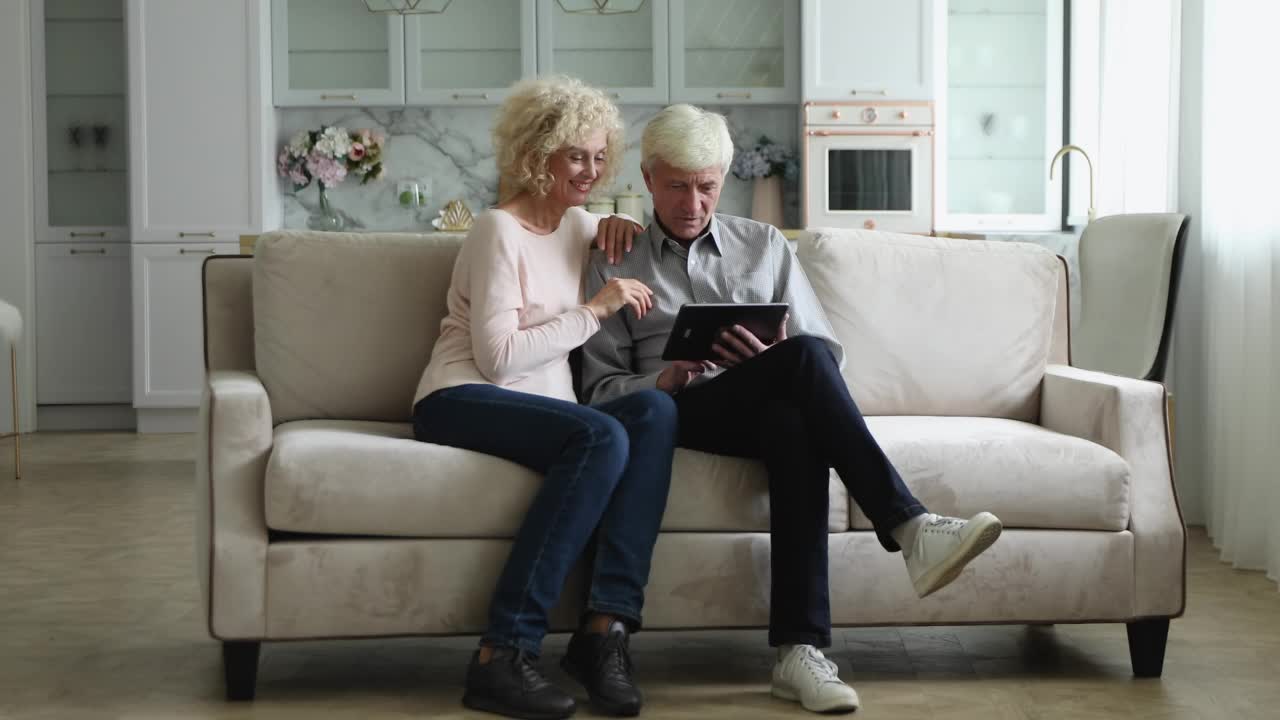 快乐的老年夫妇使用平板电脑，在沙发上放松视频素材