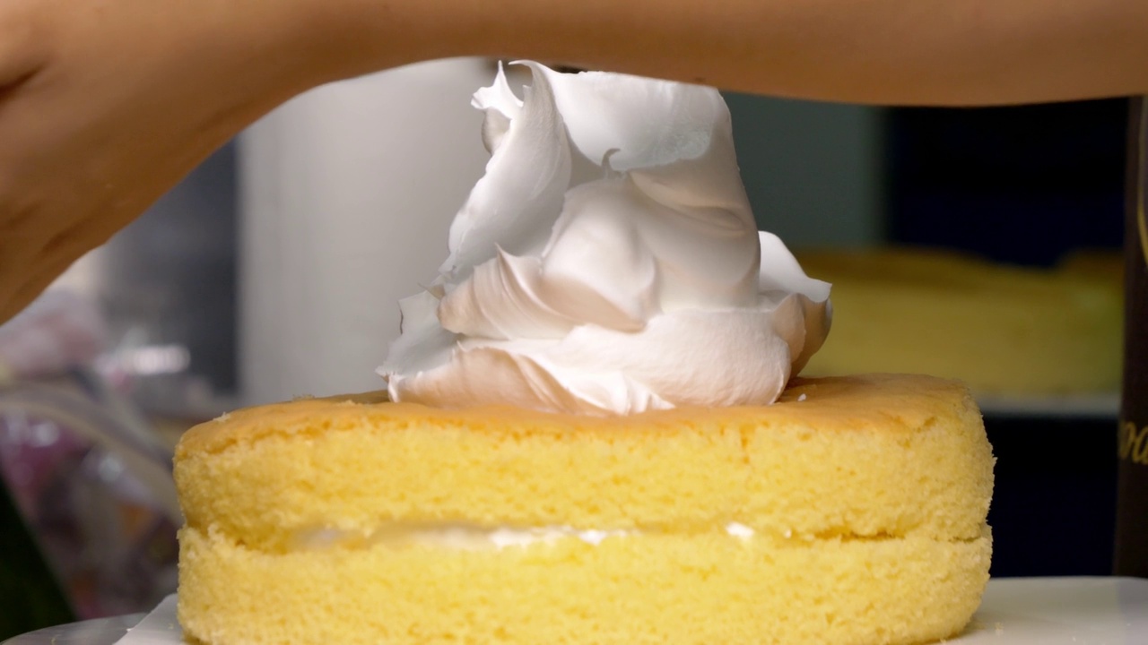 专业的糖果师在厨房里把奶油涂在蛋糕上。视频下载