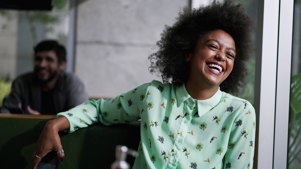 快乐的非洲裔美国女人坐在咖啡店大声笑视频下载