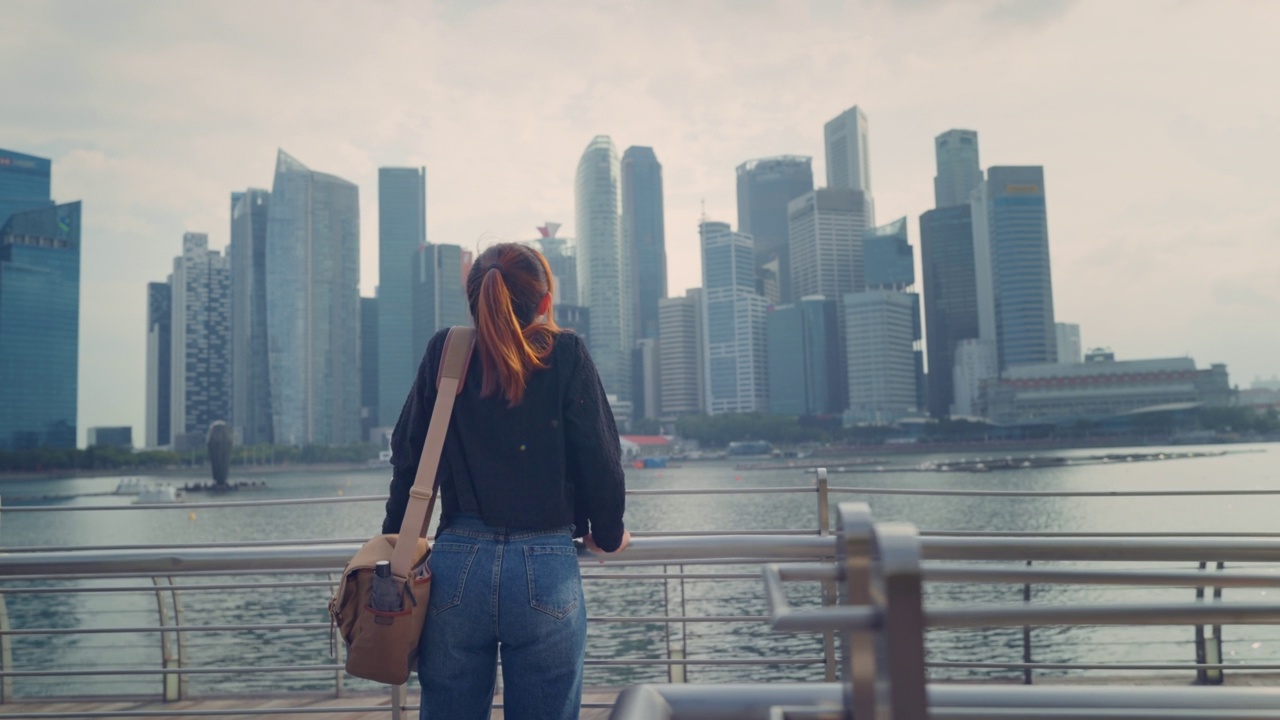 后视图年轻的游客女子放松与她的手臂抬起她的头享受新加坡城市的景色，到处去，暑假假期，慢镜头。视频素材