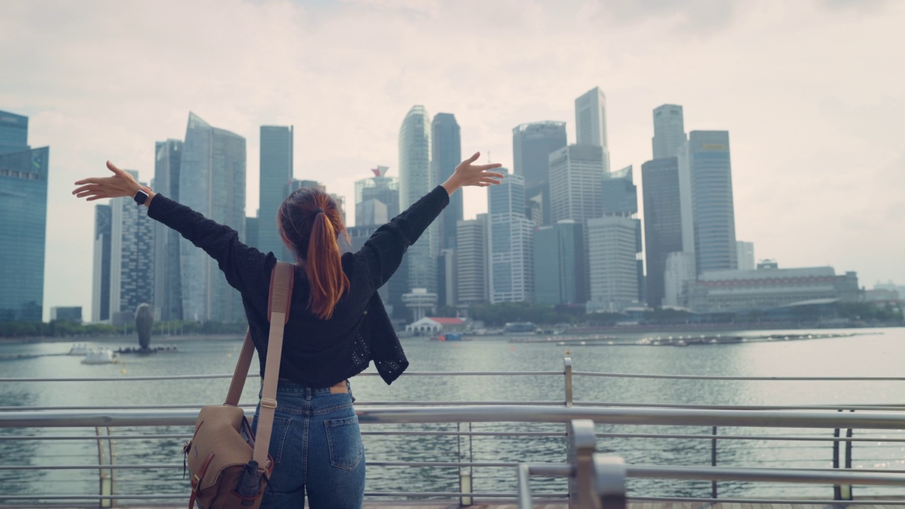 后视图年轻的女游客放松与她的手臂举到她的头，享受看新加坡城市，到处去，暑假假期，慢动作。视频素材
