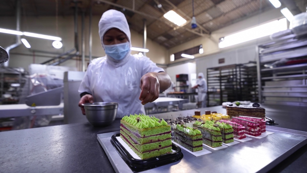 一位拉丁美洲妇女在一家工业面包店用开心果装饰美味的蛋糕视频下载