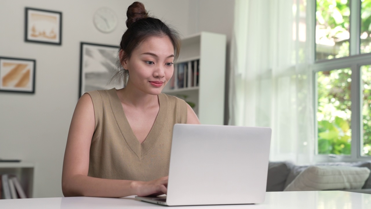 年轻的亚洲女性在家里使用笔记本电脑，看着屏幕，聊天，阅读或写电子邮件，坐在桌子上，认真的女学生做作业，在网上做研究项目。视频下载