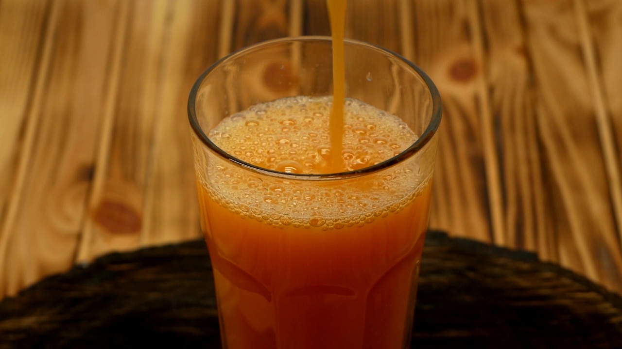 新鲜的橙汁被倒入一个木制背景的透明玻璃杯中。视频素材