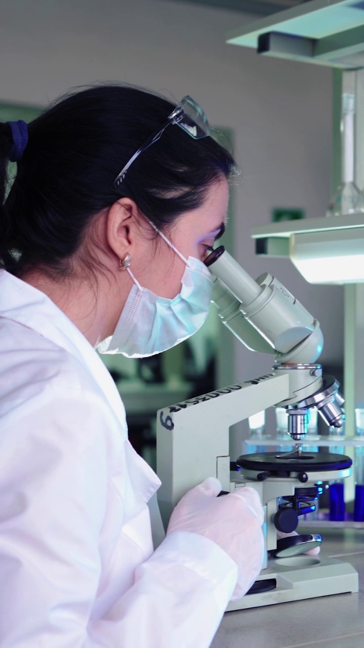 垂直视频，女微生物学家在医学科学实验室看显微镜。科学家，用高科技设备工作。药学、生物化学、科学概念视频下载