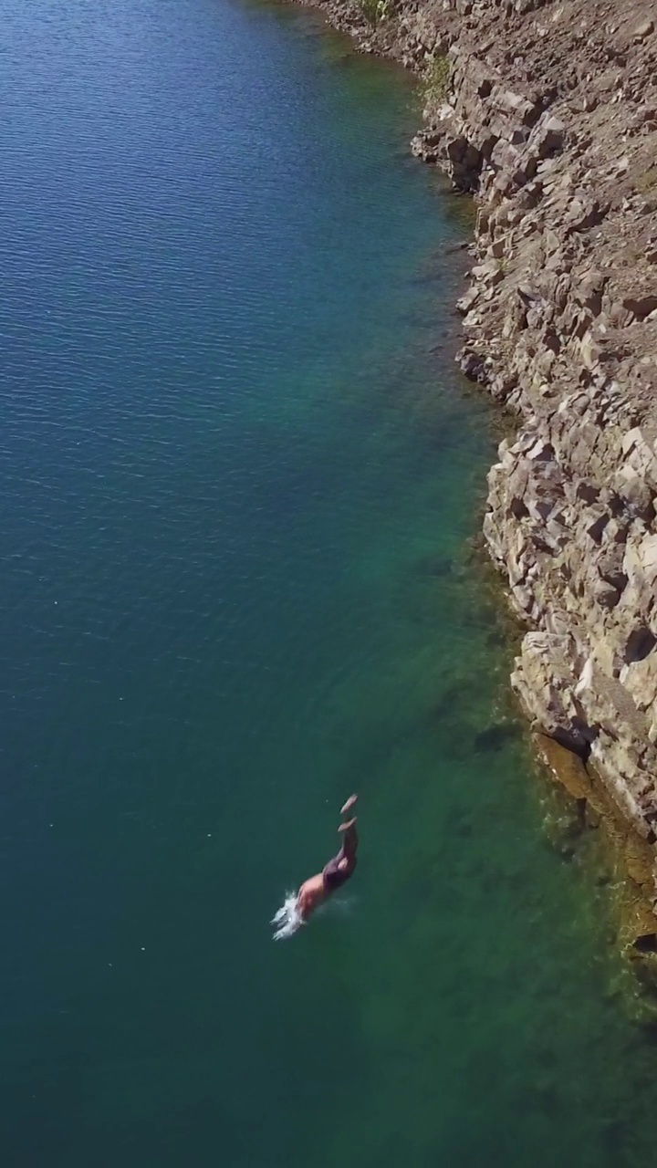 垂直视频，鸟瞰图。一个肌肉发达的男人从悬崖上跳入清澈的海水中游泳。夏天休息。俯视图视频下载