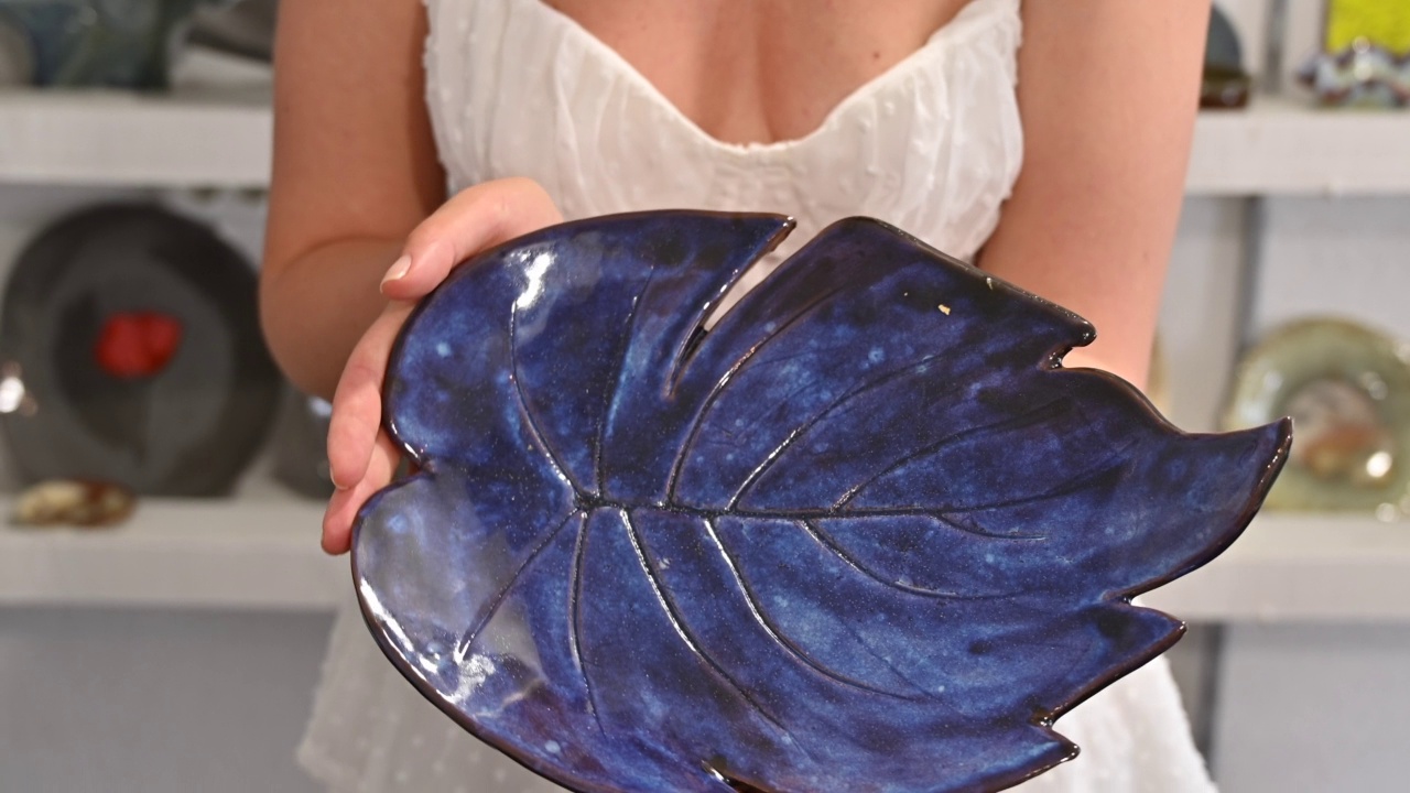 一名身穿白色连衣裙的妇女展示着一个蓝色的盘子，这是陶器作坊的最终成果视频下载