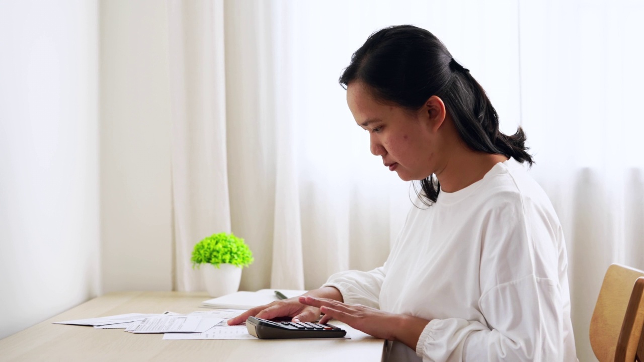 使用计算器管理家庭财务和账单的亚洲妇女。家庭财务规划视频素材