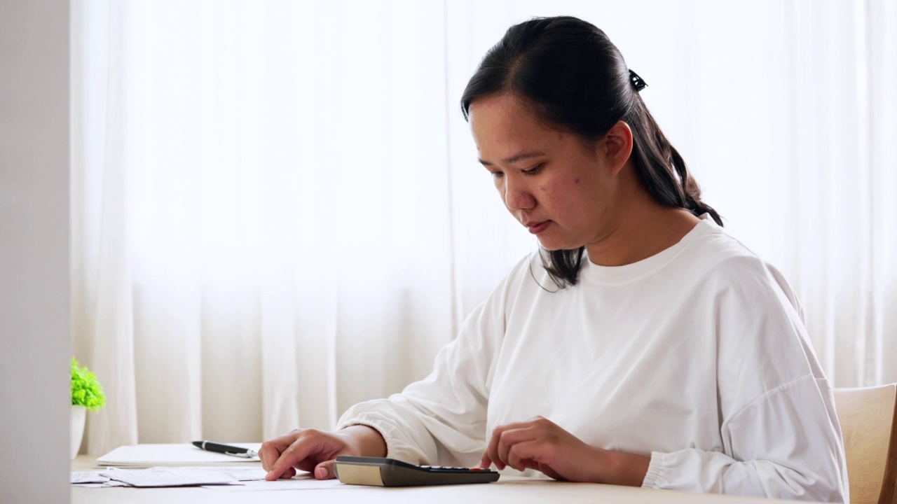 家庭理财规划与管理。年轻的亚洲妇女在家里计算家庭财务账单视频素材