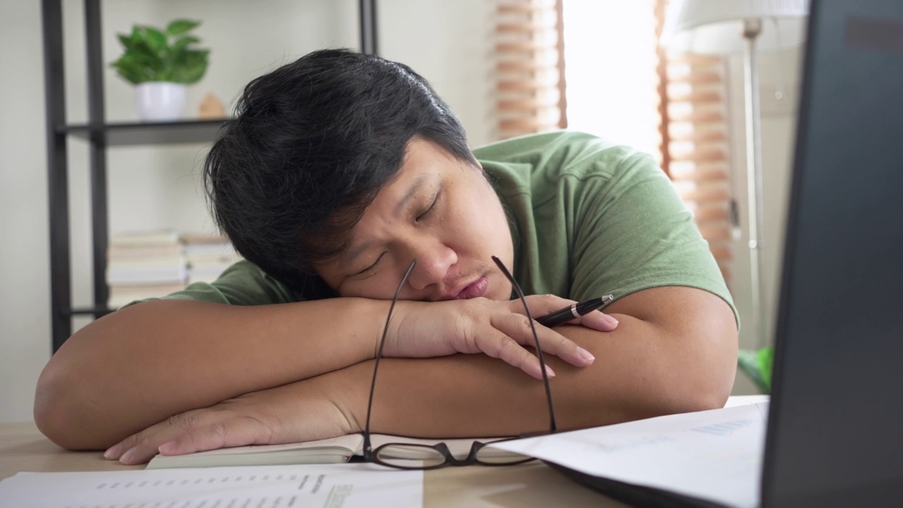 试过一个亚洲人在家用笔记本电脑工作时睡在桌子上。在自由职业中工作到最后期限视频素材