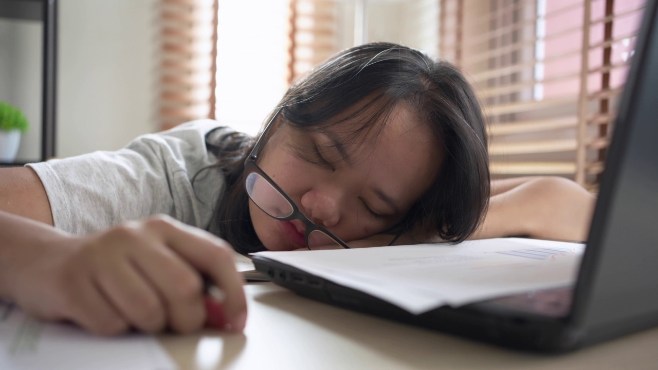 试过一位亚洲女性在家用笔记本电脑工作时睡在桌子上。在自由职业中工作到最后期限视频素材
