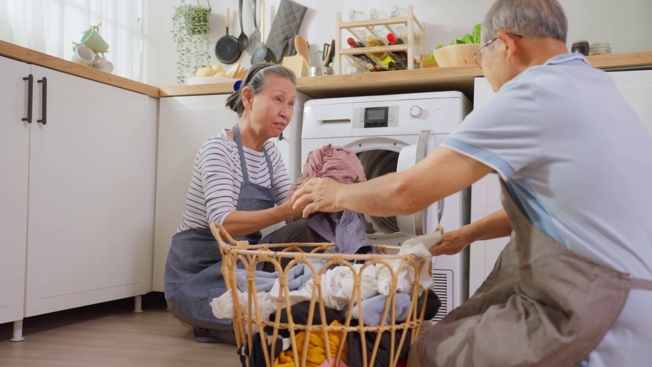亚洲老年夫妇在家里做家务和家务。积极的老人和成熟的祖父母一起打扫和把衣服放在洗衣机里洗，一起享受退休生活。视频素材