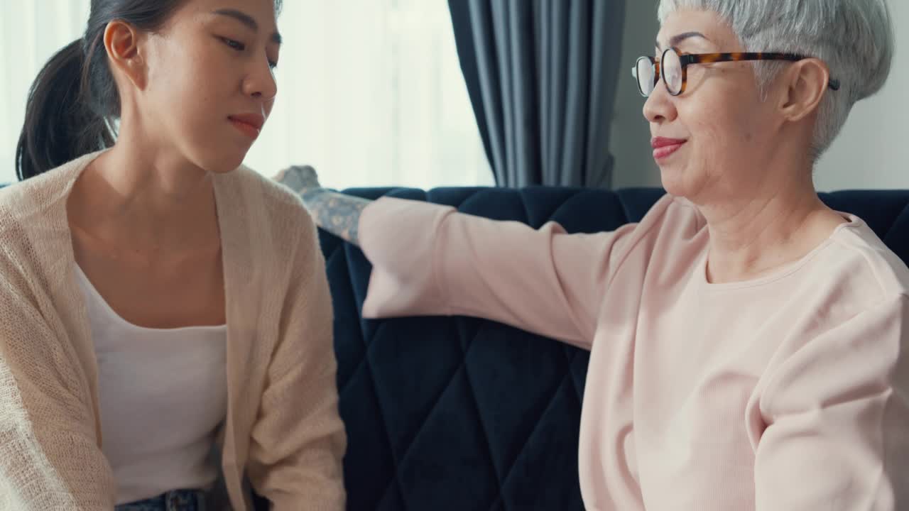 亚洲退休高级母亲坐在沙发沙发关注拥抱安慰温暖的拥抱悲伤的十几岁的女儿在家里。视频素材