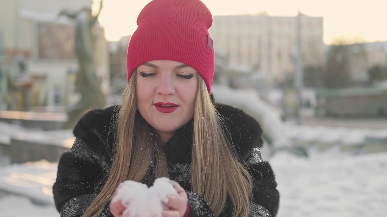 俏皮女人吹雪花在日落。年轻的女性戴着红帽子吹雪视频素材