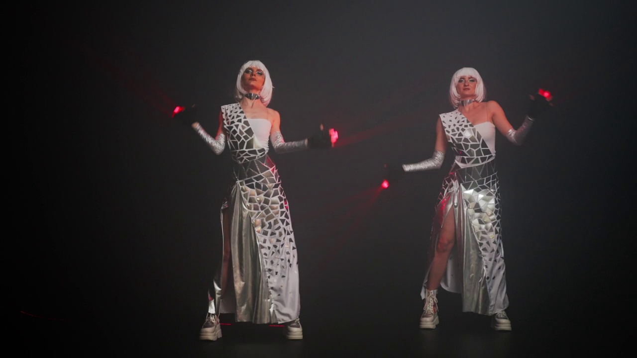 两个苗条美丽的女人穿着未来主义服装，用激光在舞台上跳舞。自信有才华的白人演员在黑人背景下跳舞。当代艺术的概念。视频下载