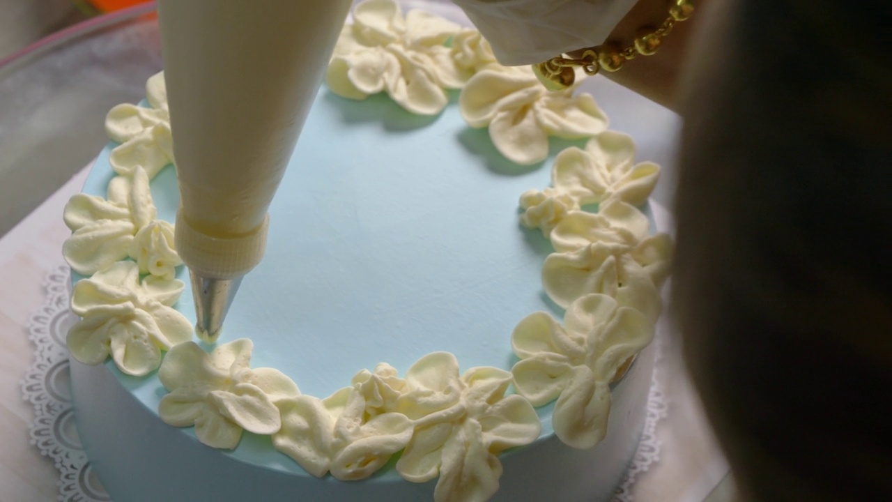 厨师慢慢地在蓝色的蛋糕上画上了白色的花朵。视频下载