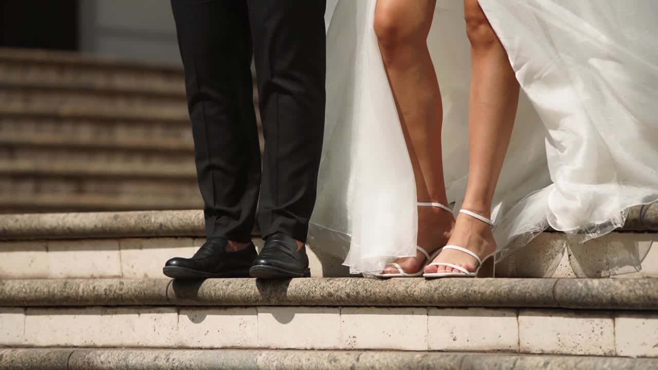 新娘和新郎走下豪华豪宅庭院的大理石楼梯。身着白衣、长纱的男女牵着手走在皇宫花园中。新婚夫妇在婚礼场地举行仪式。视频素材