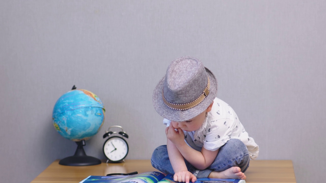 可爱的小男孩在帽子坐在桌子上阅读大书的儿童教育理念视频素材