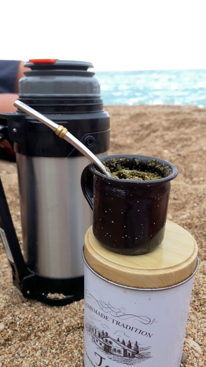 垂直视频工具包组成的便携式瓶，杯子和吸管喝美味的阿根廷mate。在海滩前放松地灌注切碎的药草。视频下载
