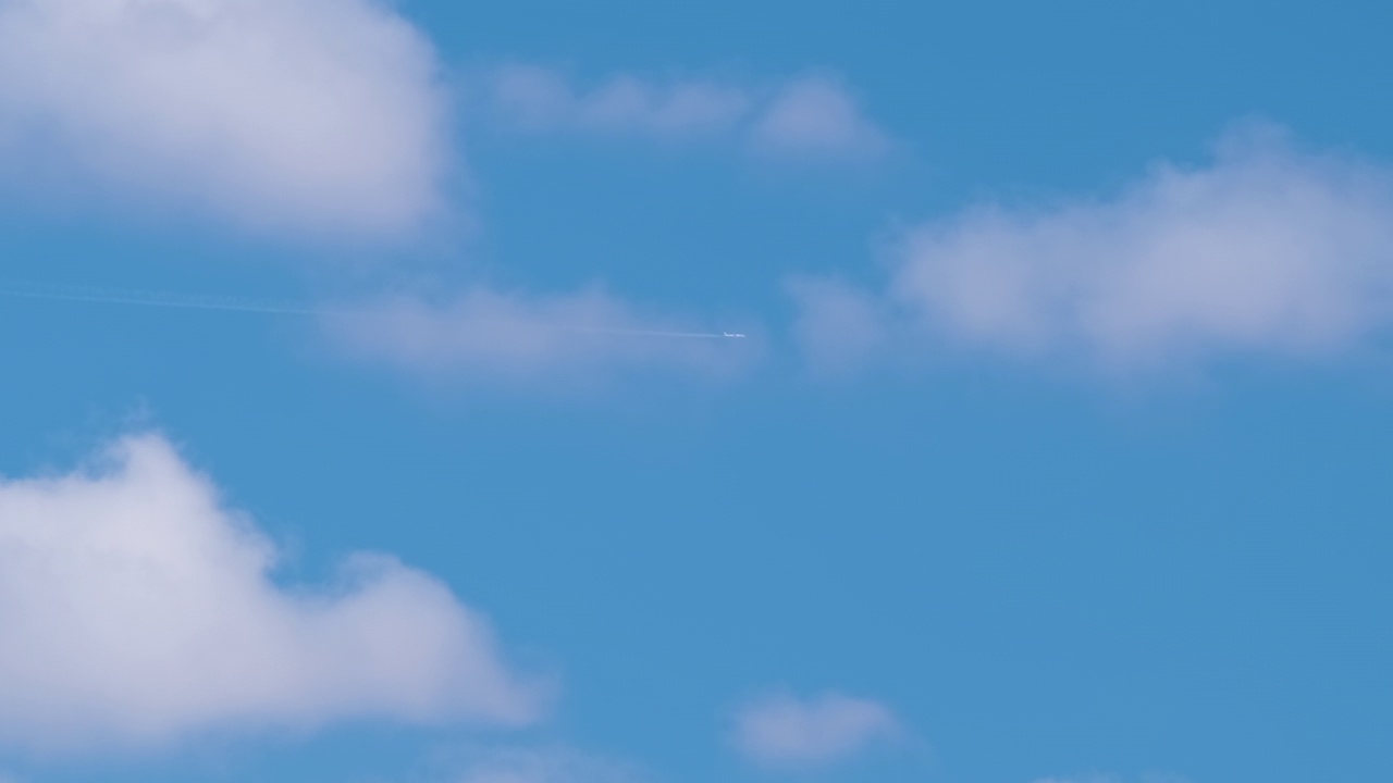 远处的喷气式客机在蓝天上高高地飞行，白云缭绕，烟雾缭绕。空中旅行的概念视频素材