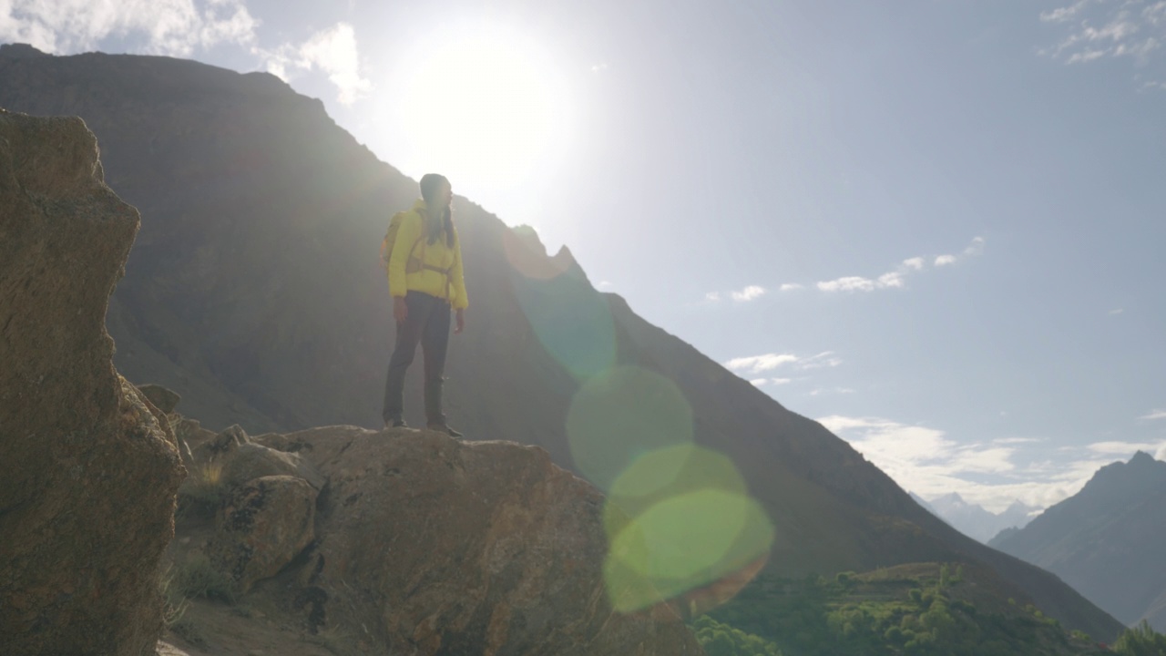 自由旅行的快乐年轻女子穿着冬装黄色站在山顶，看着早晨晴朗的天空。种族多样化的旅行者概念。与α香奈儿。视频素材