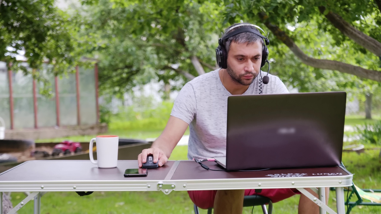 一名戴着耳机的男程序员在户外用笔记本电脑工作。视频下载