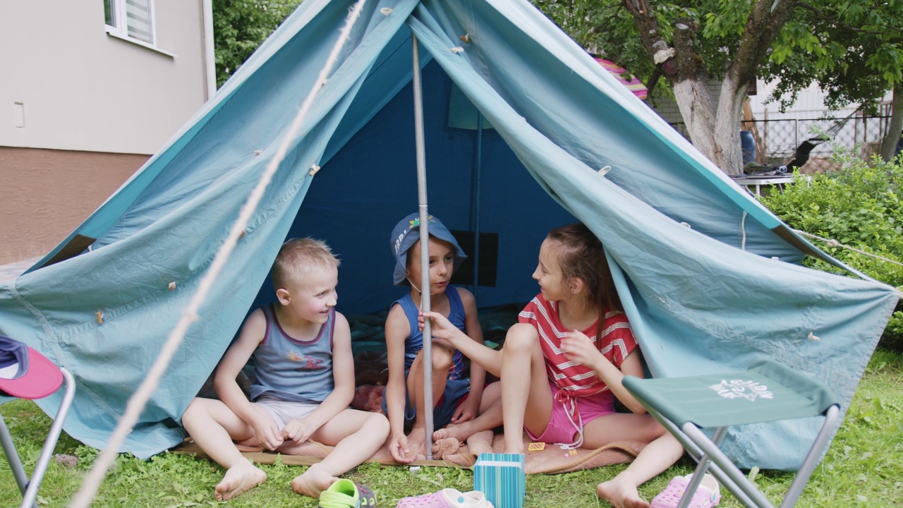 几个男孩和一个女孩坐在房子花园的旅游帐篷里。视频下载