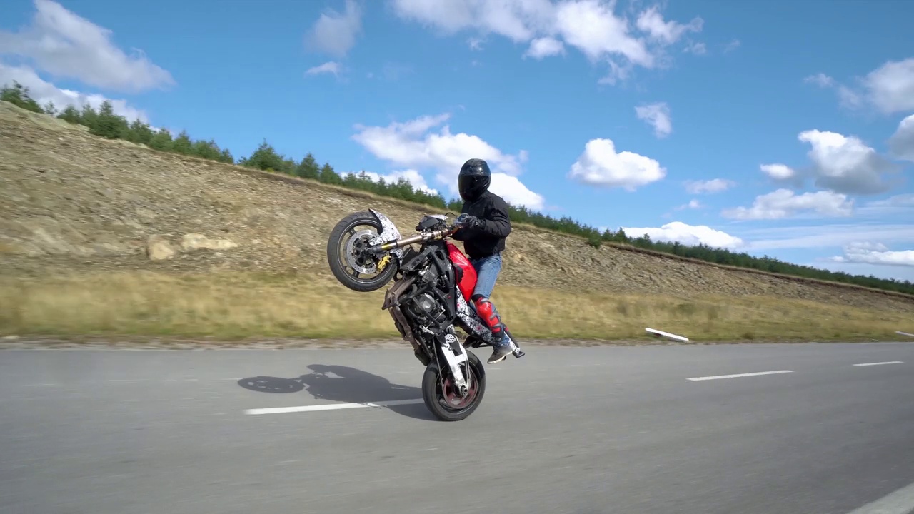 一个骑摩托车的人在空旷的山路上展示了骑摩托车后轮的特技视频下载