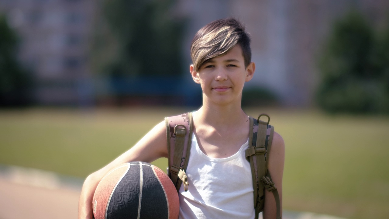 少年拿着篮球看着镜头微笑，夏日阳光灿烂视频下载