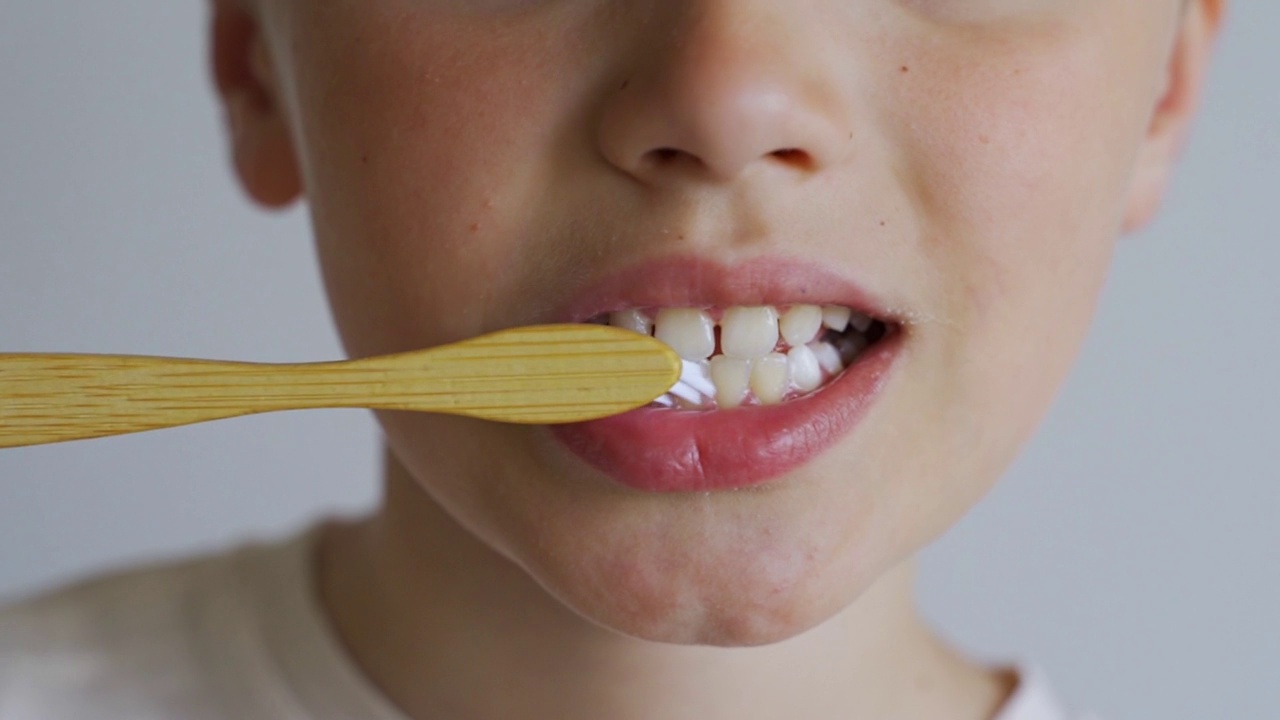 用绿色木质牙刷在白色背景上近距离观察儿童刷牙。儿童的口腔卫生，早晨的例行公事，健康的生活方式，医疗保健。视频下载