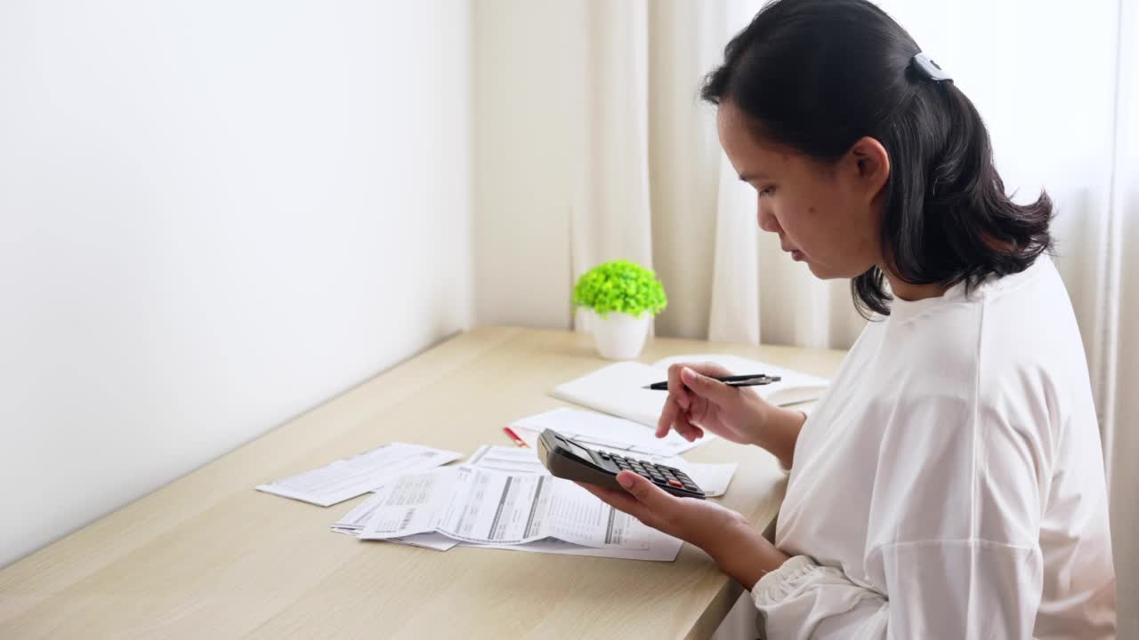 家庭理财规划与管理。年轻的亚洲妇女在家里计算家庭财务账单视频素材