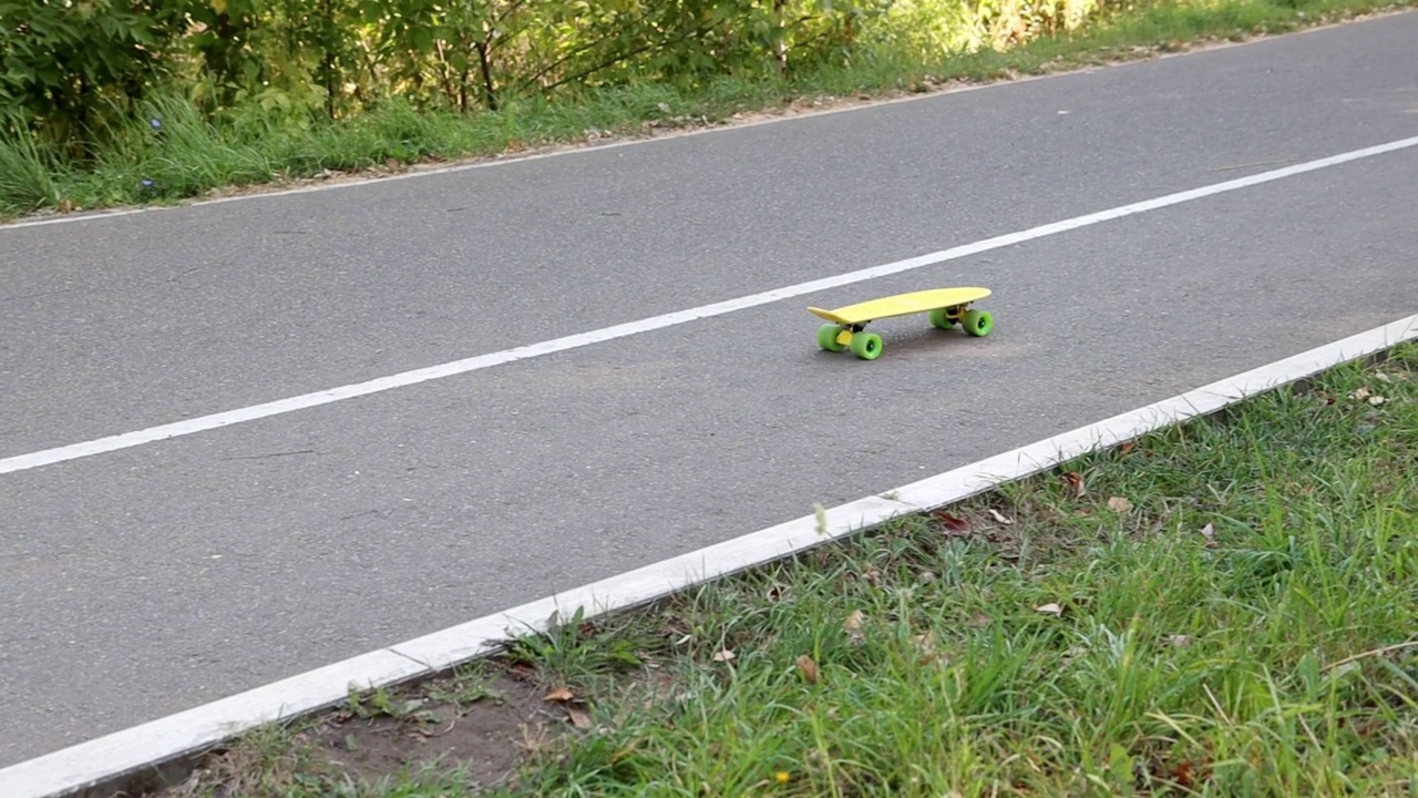 一面明黄色的滑板，绿色的轮子，在柏油路上飞快地滚动着视频素材