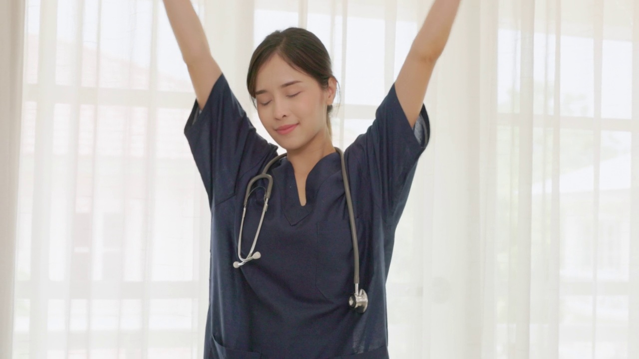 看着镜头的是一个快乐的年轻亚洲女医生，穿着白色的医疗外套，拿着听诊器。微笑的女医生在医院办公室。美丽的医院住院医生微笑着视频素材
