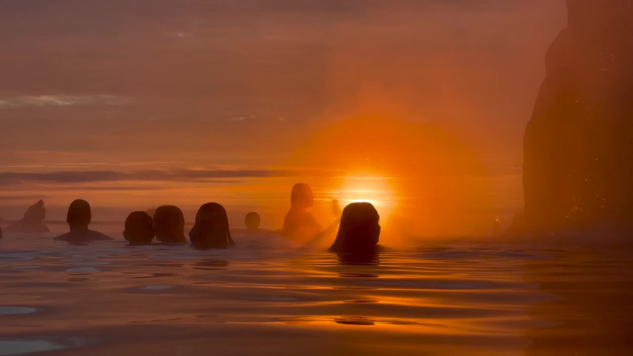 在冰岛的温泉无边泳池里，落日映照下人们的剪影。视频下载