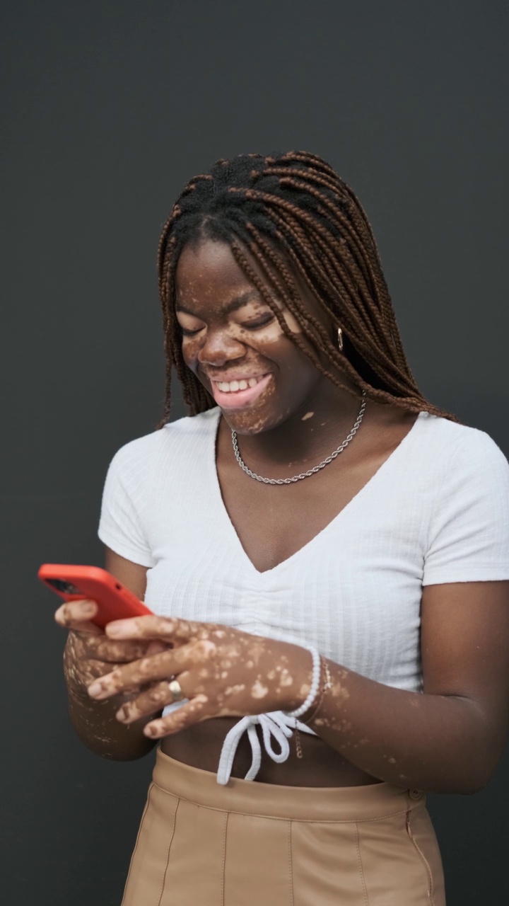年轻的非裔美国妇女白癜风微笑着使用她的智能手机。视频下载